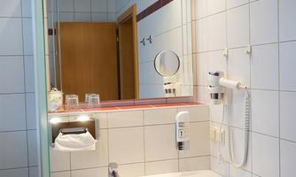 A modern bathroom with a sink, a mirror, and bright lighting. The walls are tiled, and in the background, a door is visible.