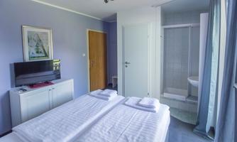 A modern bedroom with two single beds and a television. The bathroom is accessible through a door in the background.