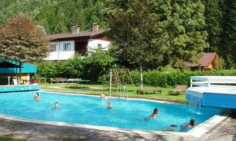 A refreshing swimming pool surrounded by greenery and trees. Several people are enjoying the swim on a sunny day.