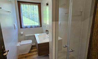 A modern bathroom with a shower, toilet, and a sink. Large windows provide plenty of natural light.