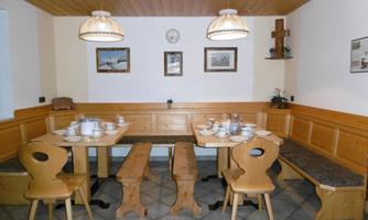 A cozy dining area with wooden tables and benches. The walls are decorated with pictures and the ceiling lights create a warm atmosphere.
