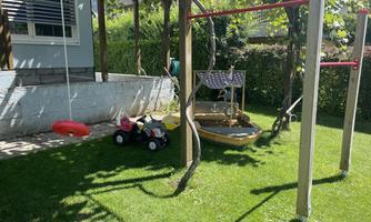 A beautiful garden with playground equipment for children. There is a swing, a Bobbycar, and a playboat.