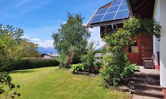A beautiful house with a solar system on the roof. The garden is green and well-kept, with a view of the mountains in the background.