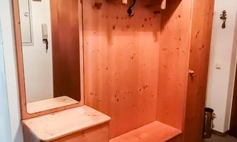 A wooden entrance cabinet with a mirror and several hooks. The cabinet has a small drawer and space for shoes.