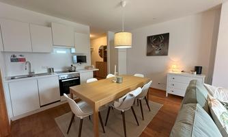 A modern kitchen with a large wooden (dining) table and comfortable chairs. The room is bright and cheerfully furnished.
