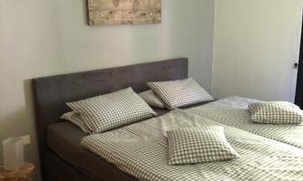 A cozy bedroom with a large bed and checkered pillows. A wooden picture hangs on the wall, and there is a small stool next to the bed.