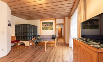 A cozy living room with a wooden ceiling and a large window. The furniture is simple and functional, with a television and a table in the center.