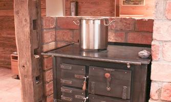 An old kitchen with a black stove and a pot on it. Next to it lies a basket of wood.