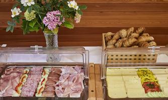 A buffet with various types of sausage and cheese. Next to it are fresh rolls and a floral arrangement.