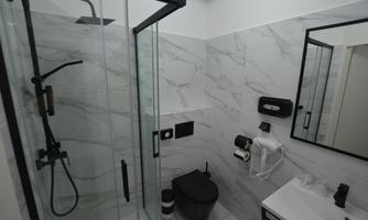 A modern bathroom with an elegant glass shower and white marble tiles. There is also a black toilet and a sink with a mirror.
