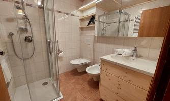 A modern bathroom with a shower, sink, and toilet. The walls are brightly tiled and the furniture is made of wood.