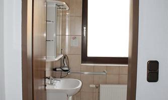 A small, simple bathroom with a sink, a mirror, and a window. The walls are decorated with tiles in neutral colors.