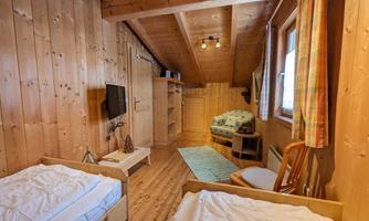 A cozy room with wooden paneling and two single beds. There is a television and a small table as well as a seating area.