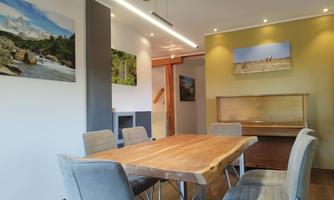 A stylish dining area with a large wooden table and gray chairs. Pictures of landscapes hang on the walls.