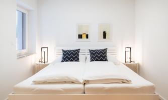 A modern bedroom with a large double bed and two bedside tables. The walls are light and there are graphic pictures on the walls.