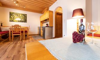 A cozy living area with a wooden ceiling and modern kitchen. The table is decorated with a wine bottle and glasses.