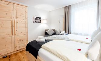 A bright and modern bedroom with two beds and a wooden wardrobe. The room has large windows and cozy decoration.