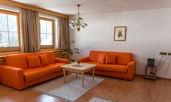 A cozy living room with two orange sofas and a small table.  
Large windows provide plenty of daylight and an inviting atmosphere.