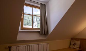 A cozy room with a slanted window. Through the window, the mountains and a church tower are visible.