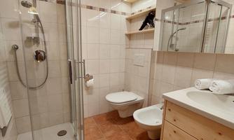 A modern bathroom with a shower, sink, and toilet. The walls are brightly tiled, and wooden shelves provide additional storage space.