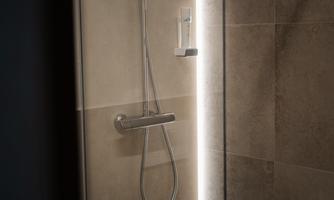 A modern shower with a glass wall and elegant tiles. The showerhead is stylish and the lighting creates a pleasant atmosphere.
