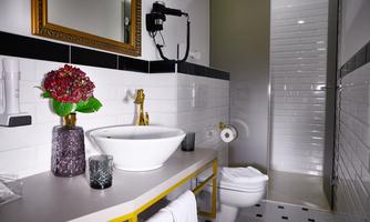 A modern bathroom with white tiles and elegant decor. It features a stylish sink, a golden faucet, and a shower in the corner.