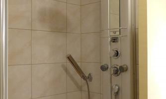 Tiled shower with rain shower head, handheld shower and shower panel with massage jets and controls.