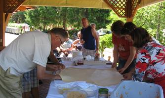 A group of people working together at the table. They are preparing a dough base and seem to be having fun.