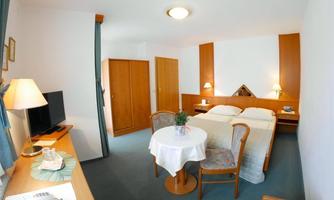 A cozy room with a double bed, a table, and two chairs. The television and a bedside lamp complete the amenities.