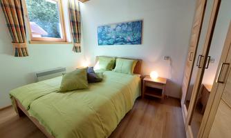 A cozy bedroom with a double bed and green bedding. A large window provides plenty of daylight and a pleasant atmosphere.