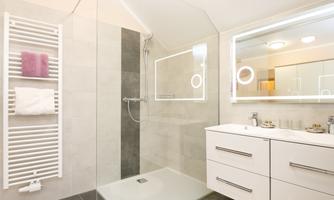 A modern bathroom with a shower cabin and a sink. The walls are light and there are practical towel holders.