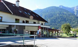 A rustic building with a red entrance and a large roof. In the background, green mountains stretch under a clear blue sky.