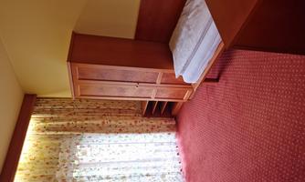 A simple room with a bed, a wardrobe, and a window with curtains. The floor is covered with red carpet.