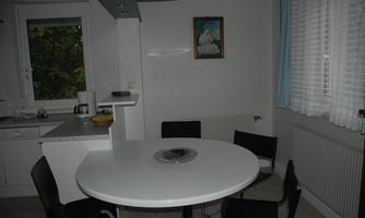 A modern kitchen with a round white table and black chairs. There is a picture hanging on the wall, and there is a window with a view to the outdoors.