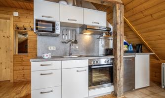 A modern kitchen with white cabinets and wooden paneling. It is equipped with a stove, a microwave, and a sink.
