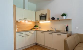 A modern kitchen with bright furniture and elegant appliances. On the countertop, there are some fresh ingredients and a bottle of wine.