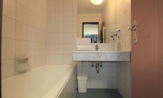 A small, bright bathroom with a bathtub and a sink. It features white tiles and a simple, modern decor.
