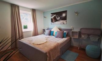 A modern bedroom with a large bed and soft colors. The windows let in plenty of daylight and contribute to the cozy atmosphere.
