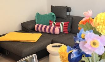 A modern living room with a gray sofa and colorful cushions. On a table, there are vibrant flowers in a vase.