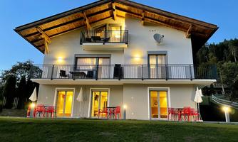 A modern house with several balconies and terraces. It is surrounded by a well-kept garden and looks inviting in twilight light.
