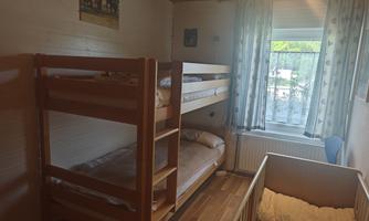 A cozy room with a bunk bed and a children's bed. The room has a window with a view outside and bright wooden walls. Wardrobe.