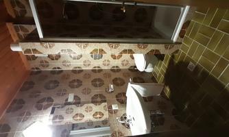 A bathroom with a shower, a toilet, and a sink. The walls are decorated with patterned tiles and the ceiling is made of wood.