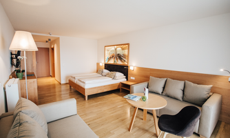 A modern room with a cozy sofa and a round table. There are two beds and beautiful wooden details on the wall.
