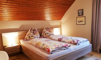 A cozy bedroom with a double bed and colorful cushions. The wood paneling and soft lighting create a warm atmosphere.