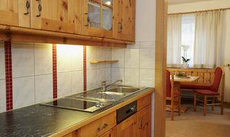 A cozy kitchen with wooden cabinets and a modern sink. In the background, there is a dining area with a table and chairs visible.