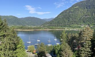 A clear lake surrounded by green mountains and trees. Sailboats are peacefully resting on the water.