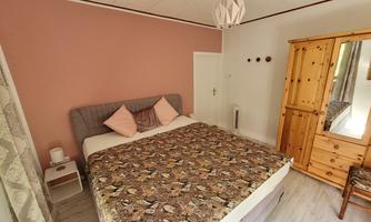 A cozy bedroom with a large bed and a decorative bedspread. In the room, there is a wardrobe and a nightstand.