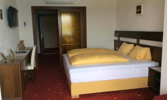 A cozy room with a double bed and yellow cushions. There is a desk and a TV on the wall.