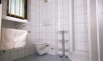 A clean bathroom with white tiles. It contains a shower, a sink, and a toilet.