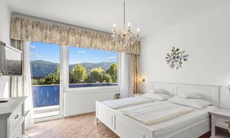 A bright bedroom with a large window and a view of the mountains. The room is elegantly furnished with a double bed and a modern television.